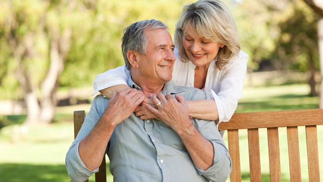 Senior woman hugging her husband who is on the bench